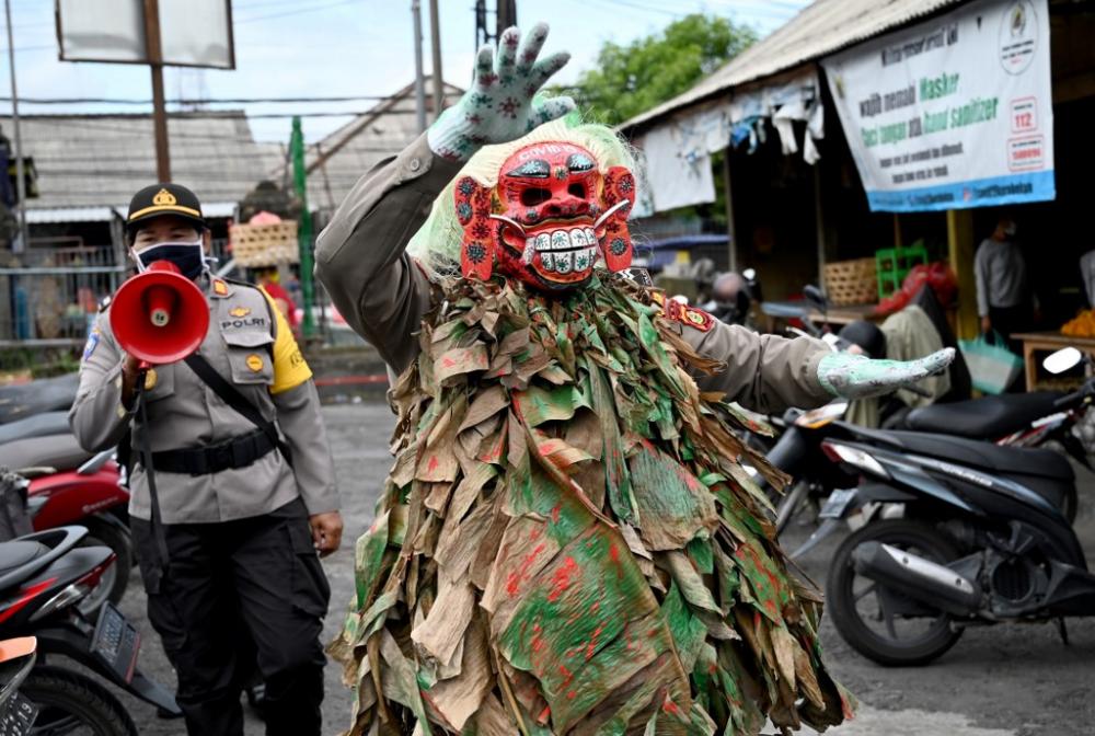A Bali police officer wears a scary mask called "Leak" while trying to educate people on COVID-19 coronavirus matter at a traditional market in Kerobokan, near Denpasar on May 14, 2020