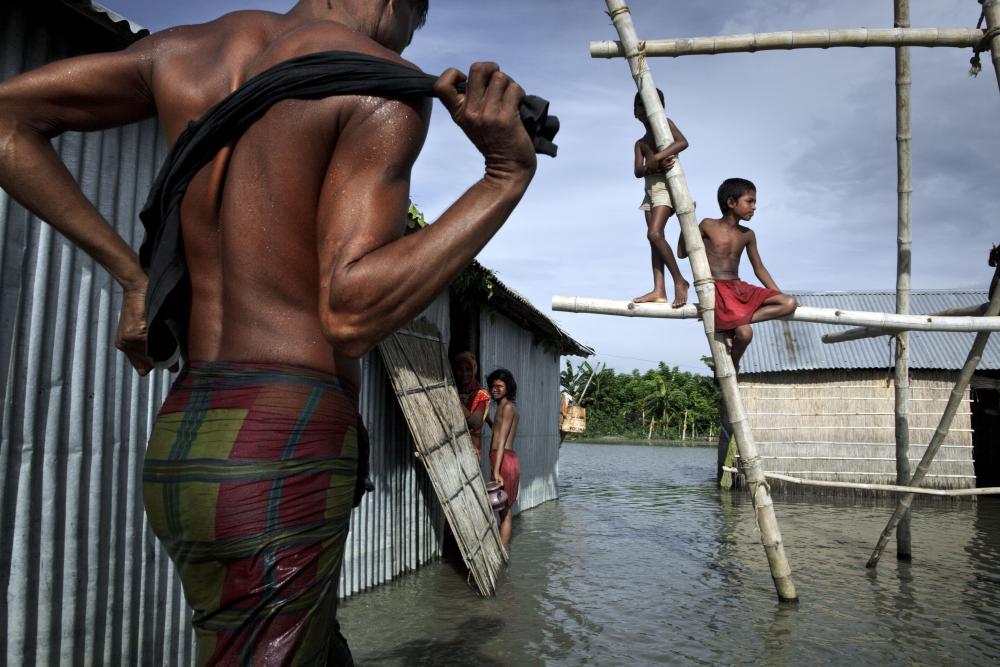 This image shows a family coping with seasonal flooding by building this wooden structure to climb on and stay dry when the water runs deep. It was taken in the Gaibandha District, Bangladesh, by photographer Jonas Bendiksen in 2010